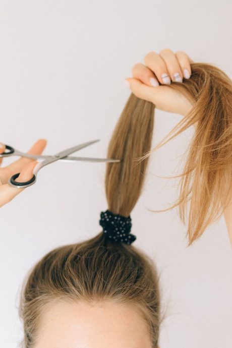 Close-up of scissors cutting long hair indoors, highlighting hairstyling process.